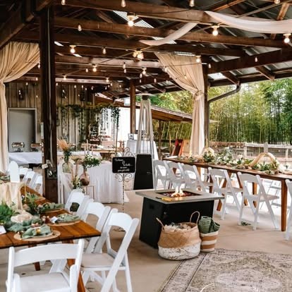 Rustic barn wedding reception with white chairs, string lights, draped fabric and greenery