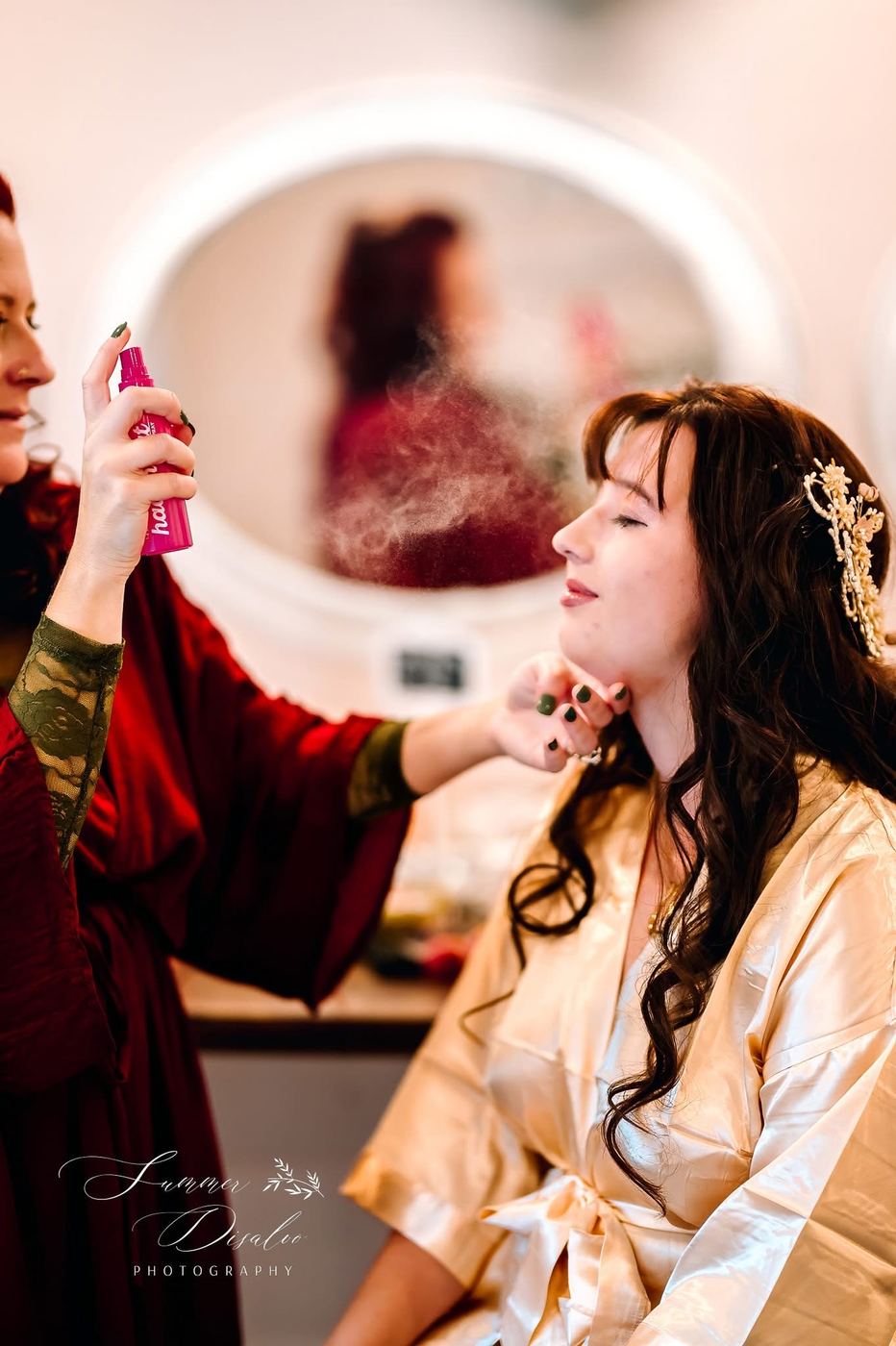 Bride getting ready as her hair is finished with setting spray (photographer watermark shown)