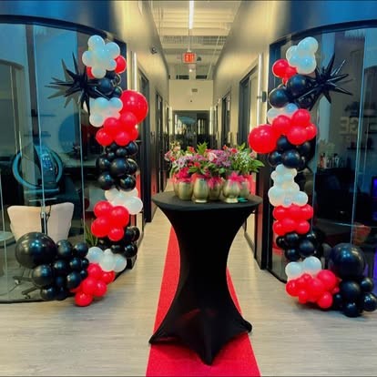 Red, black and white balloon garland framing a hallway with a red carpet and floral cocktail table