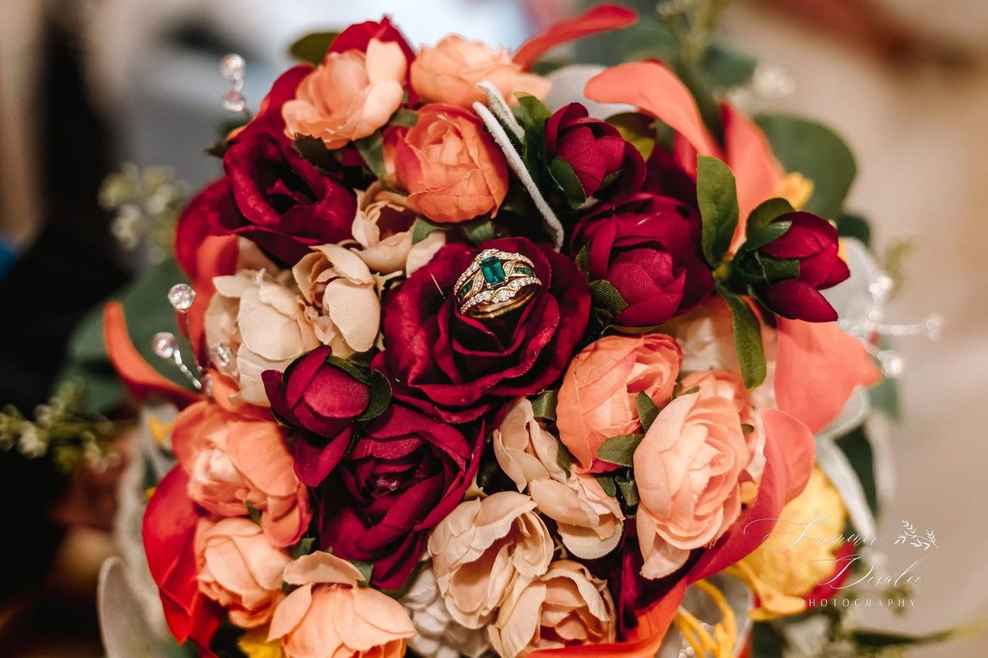 Autumn bridal bouquet of burgundy, peach and ivory roses holding an emerald and diamond ring set (photographer watermark shown)