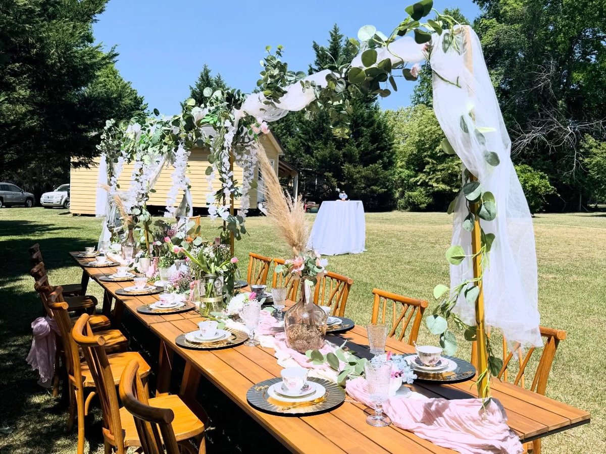 Garden party long table under a greenery and tulle arch on a sunny lawn