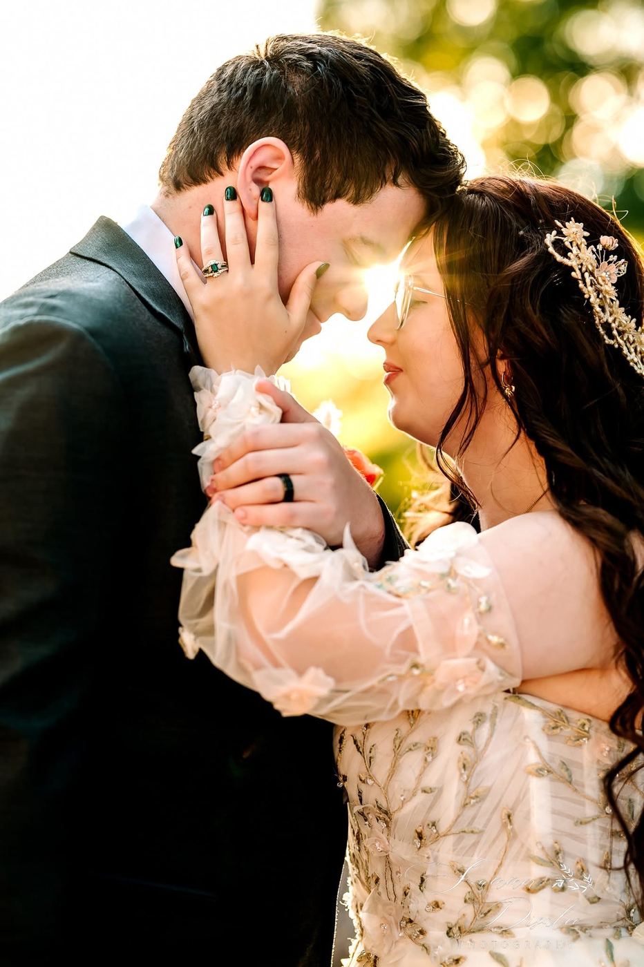 Couple embracing forehead to forehead in golden-hour light, showing the emerald ring (photographer watermark shown)