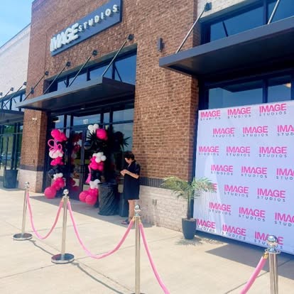 Storefront grand opening with pink, white and black balloon columns and a branded step-and-repeat backdrop