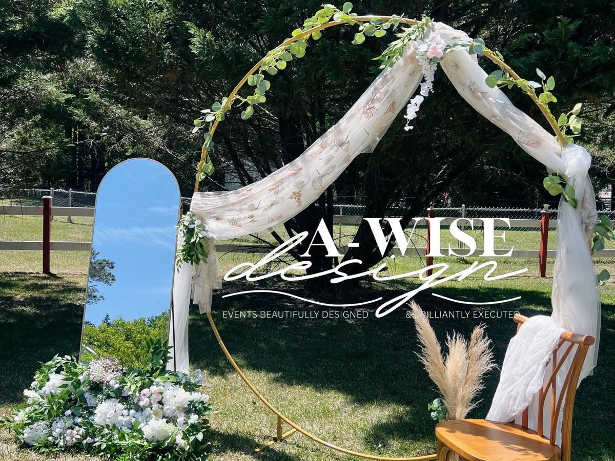 Gold hoop arch draped in butterfly tulle with greenery, florals, an arched mirror and a wooden chair