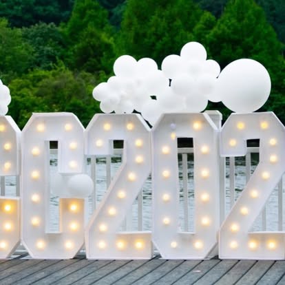 White light-up marquee numbers topped with white balloons on a waterfront deck