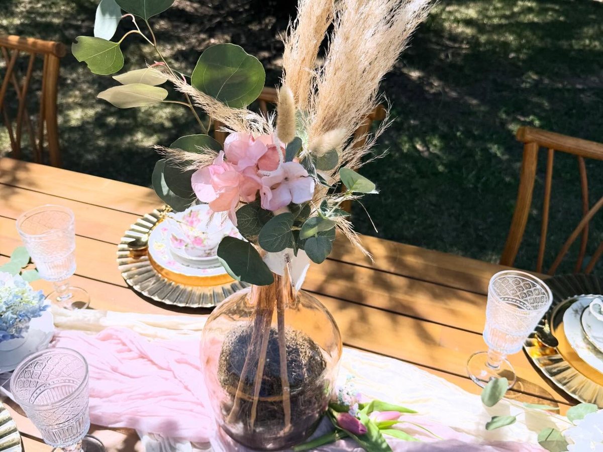 Pampas grass, eucalyptus and pink hydrangea centerpiece in a blush glass vase on a garden table