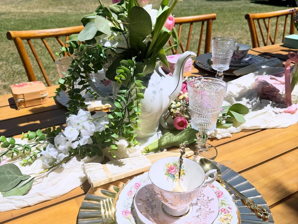 Vintage teapot centerpiece with tulips and greenery beside a rose teacup on a gold charger
